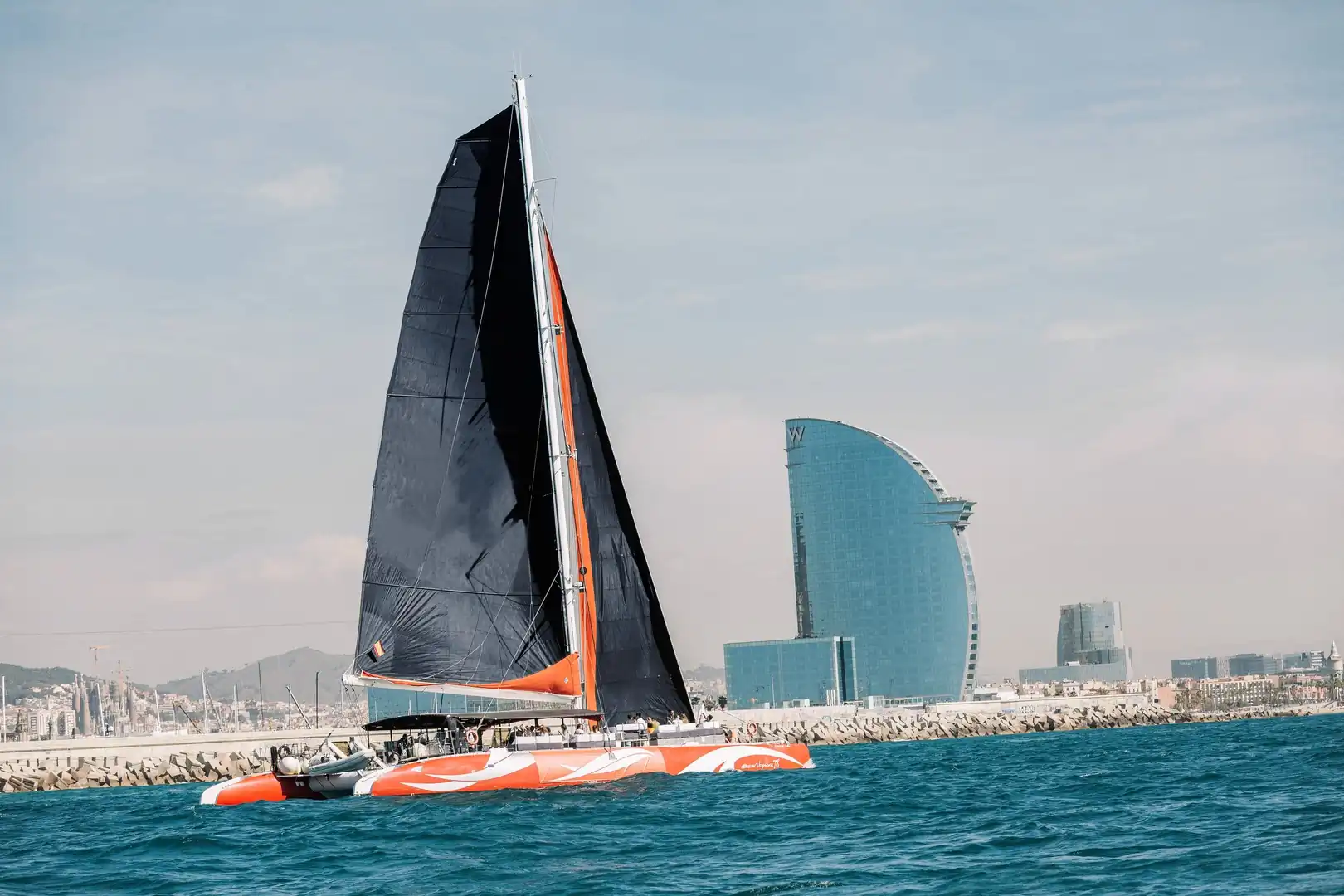 Catamarán oceánico de vela negra navegando junto al Hotel W de Barcelona