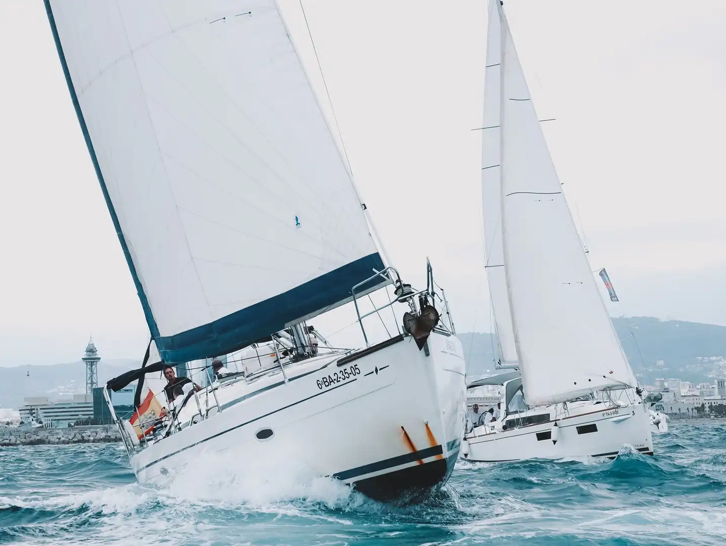 Dos veleros compitiendo escorados entre las olas durante una regata corporativa