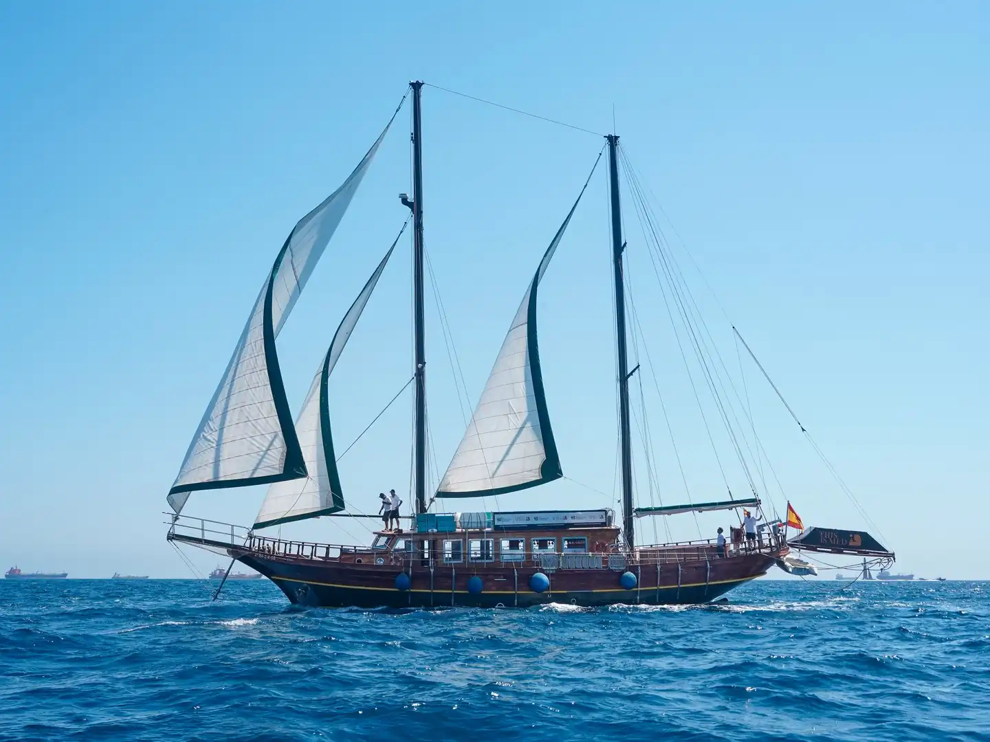 Goleta de madera de dos mástiles navegando a vela con tripulación a bordo y bandera española