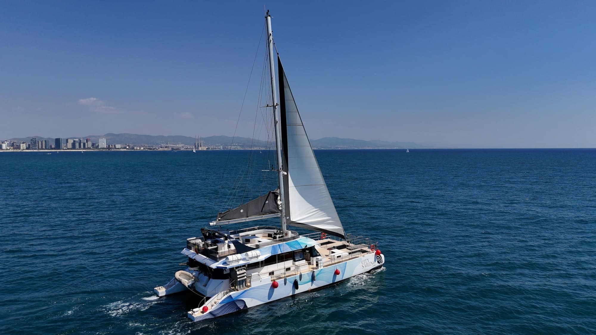 Catamarán City Sailing navegando a vela con la costa de Barcelona al fondo