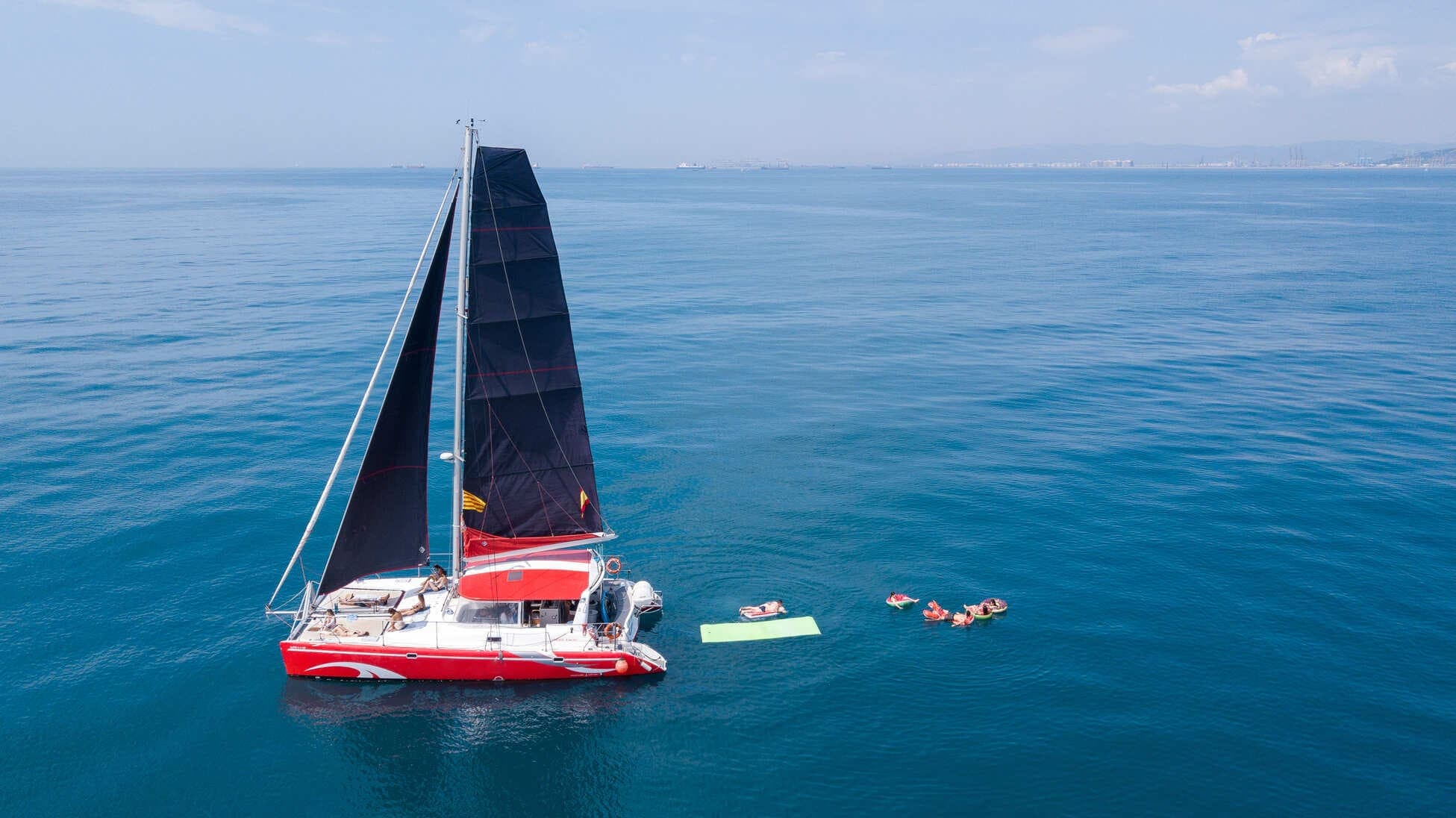 Vista aérea de catamarán fondeado con bañistas relajándose en flotadores junto al barco